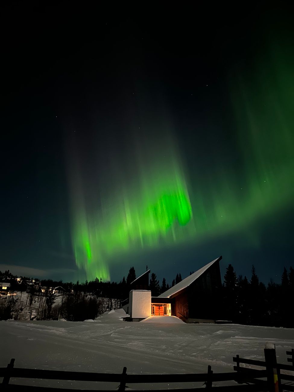 Minimalist black cabin under green northern lights on snow-covered coast
